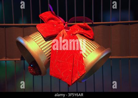 a charming metallic gold Christmas bells adorned with a vibrant red bow, suspended in a warm and inviting interior space featuring wooden paneling and Stock Photo