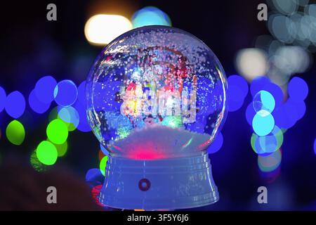a close-up of a snow globe spinning at night, adorned with bokeh lights, on a white and red background, holiday decorations and festive celebrations. Stock Photo