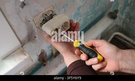 raftsman's hands are used to removing or installing an old double-wall socket. Using a yellow-and-black-handled screwdriver Stock Photo