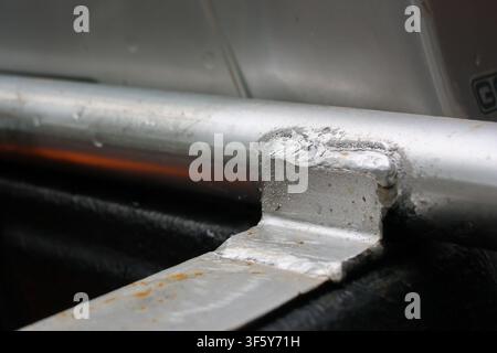 An aluminum metal joint with rough weld on tubular railing and flat bracket, close up detail showing texture, corrosion spots and industrial finish co Stock Photo