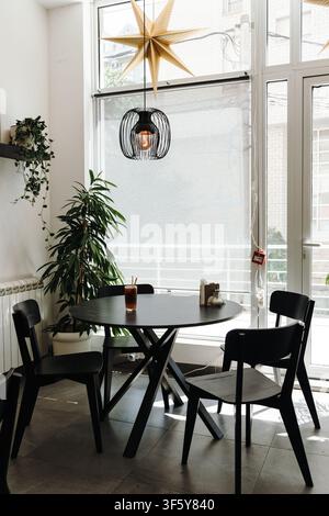 Bright modern cafe interior featuring an iced coffee on a round table by the window. Minimal design with natural light and cozy atmosphere. Stock Photo