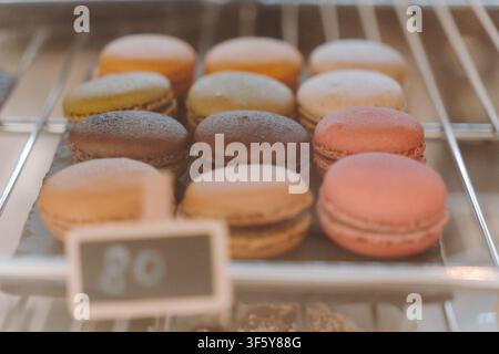 Assorted French macarons displayed in a refrigerated bakery showcase. Soft pastel colors create an elegant dessert presentation. Stock Photo