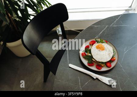 Top view of avocado toast topped with a fried egg and fresh vegetables on a modern cafe table. Clean composition with dining accessories and copy Stock Photo