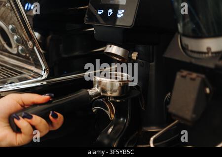 Barista grinds fresh coffee beans directly into a portafilter before brewing espresso. Close-up of professional coffee preparation in a modern cafe. Stock Photo