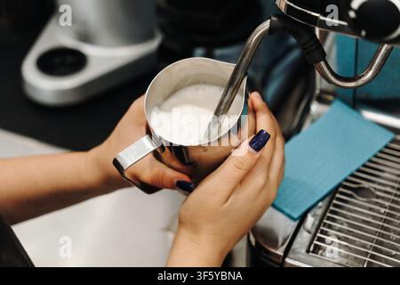 Barista steams fresh milk with a professional espresso machine before preparing a coffee drink. Close-up of the milk frothing process. Stock Photo