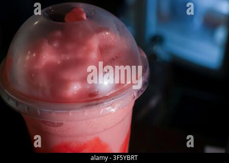 A pink milkshake topped with whipped cream under plastic dome lid in low light evoking cozy indulgence Stock Photo