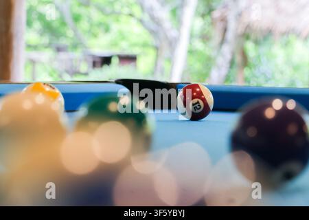 A red and white numbered pool ball on blue felt near pocket with blurred other billiard balls in foreground creating relaxed game atmosphere Stock Photo