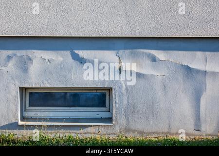 Old Building Wall With Peeling Surface Cracks and Small Basement Window Stock Photo