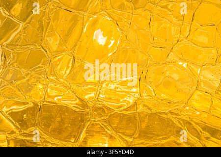 Abstract close-up of translucent golden yellow textured glass with organic irregular patterns, highlights and layered reflections. Suitable for luxury Stock Photo