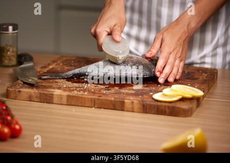 Chef descaling fresh sea bream in kitchen Stock Photo