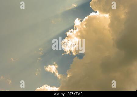 Bright sunlight streams through large golden clouds, creating visible rays against a blue sky. Stock Photo