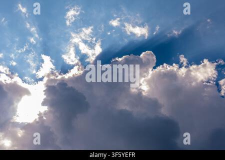 Bright sunlight shines from behind large dramatic clouds against a deep blue sky. Stock Photo
