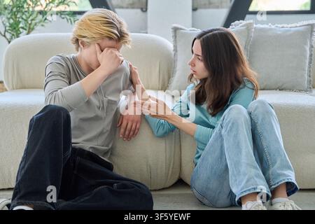 Young woman comforts upset boyfriend after conflict, sitting on living room floor Stock Photo