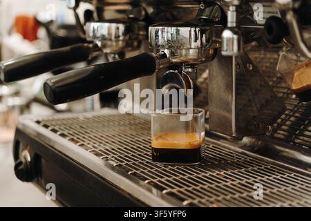 Fresh espresso flowing from a professional coffee machine into a glass container during extraction. Rich crema forming in a specialty cafe. Stock Photo