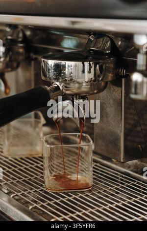 Fresh espresso flowing from a professional coffee machine into a glass container during extraction. Rich crema forming in a specialty cafe. Stock Photo