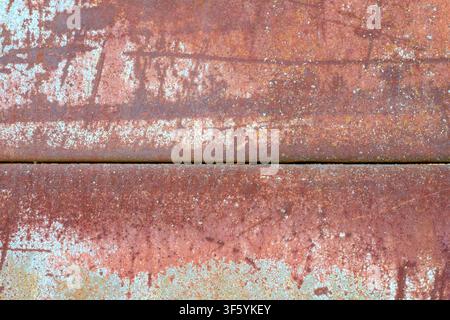 Weathered and oxidized rusty iron sheet with peeling paint traces and horizontal seam. Concept of industrial decay, aging, and grunge background. Stock Photo