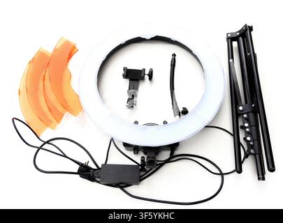 A topdown view shows a disassembled ring light kit including the ring light, tripod, orange filters, phone mount, and power cables on a white backgrou Stock Photo