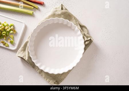 Empty ceramic pie dish with fresh rhubarb ingredients on white kitchen background Stock Photo
