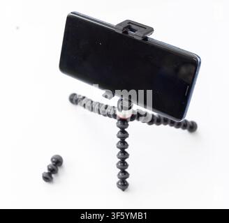 A smartphone is securely mounted in a horizontal position on a small, flexible tripod on a plain white background Stock Photo