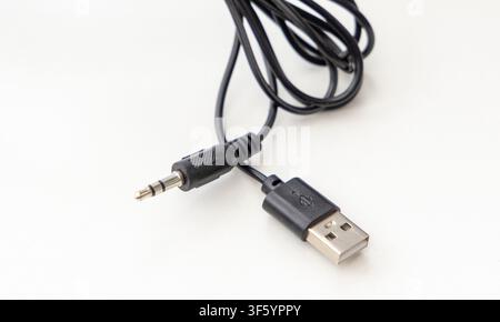 A black USB cable with an audio jack connector is displayed against a plain white background Stock Photo