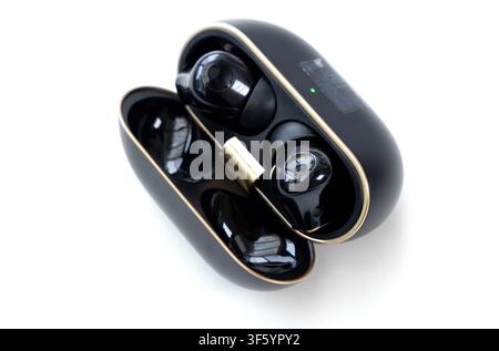 A pair of modern black wireless earbuds rest inside their open charging case against a plain white background Stock Photo