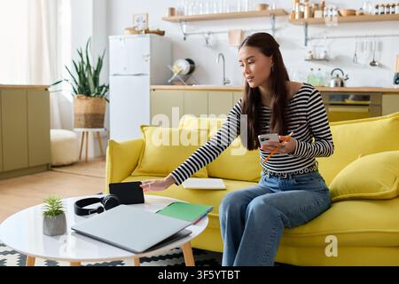 Focused on her tasks, a young woman works remotely from her cozy apartment Stock Photo