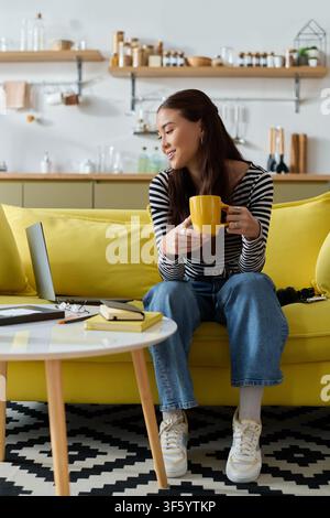 Focused young woman works remotely from her stylish apartment while sipping coffee Stock Photo