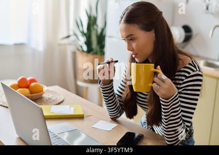 A young asian woman works remotely from her cozy apartment, focused on her tasks Stock Photo