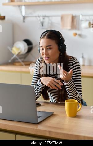 A young Asian woman works remotely on her laptop in her cozy apartment, having video call Stock Photo