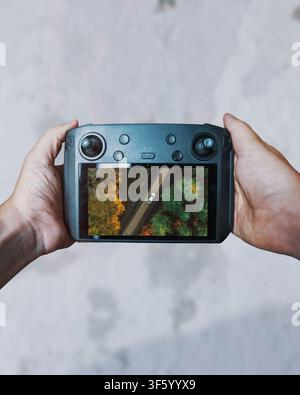 First person view of a drone remote controller displaying an aerial shot of a white car driving through a forest. Ideal for drone technology. Stock Photo