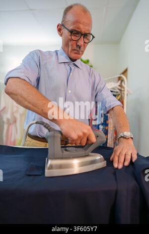 Experienced tailor concentrating on ironing fabric in a workshop, focusing on precision and craftsmanship in garment production Stock Photo