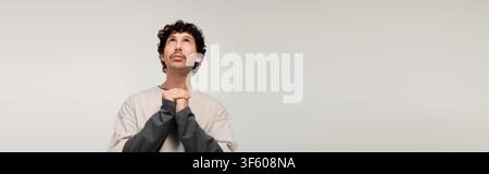 A handsome young man stands with hands clasped, looking up and celebrating Movember. Stock Photo