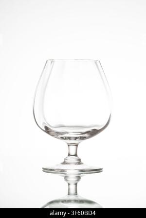 Clear empty brandy glass sitting on a reflective white background Stock Photo