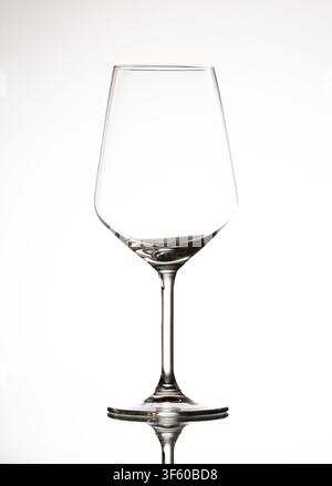 Empty clear crystal wine glass standing on a reflective surface against a white background Stock Photo