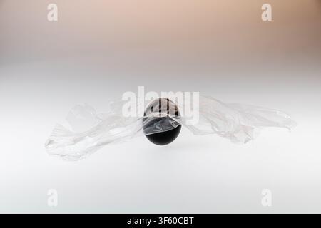 Wide horizontal studio still life of a single black painted egg with transparent plastic film on a white background, with very generous copy space on Stock Photo