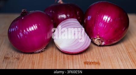 Close-up of three red onions on a cutting board, with half an onion in the foreground. Close-up of three red onions on a cutting board, with half an o Stock Photo