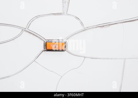 Close-up detail of cracked and peeling white vehicle body coating or vinyl wrap with a small orange rectangular side marker light reflector. Concept of paint damage, old transport maintenance, aging material, and automotive repair. Stock Photo