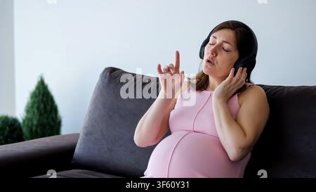 Pregnant woman enjoying music, singing and relaxing at home Stock Photo