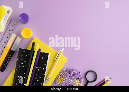 Stationery items including notebooks, pens, markers, ruler, stapler, magnifying glass, and paper clips arranged on a pastel purple surface. Bright, cl Stock Photo