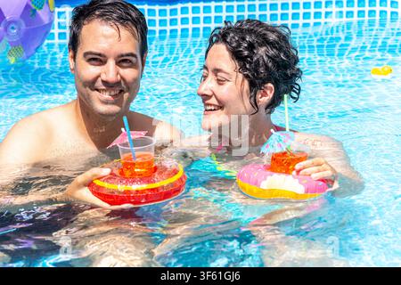 Happy couple enjoying summer vacation in swimming pool with drinks Stock Photo