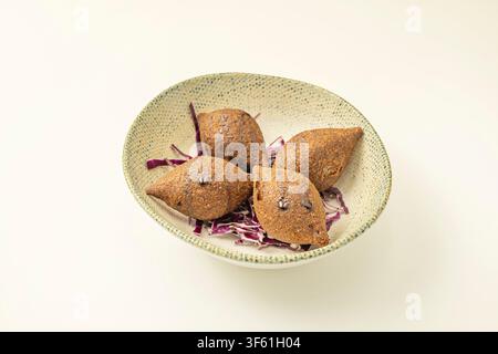 Fried kibbeh croquettes on shredded red cabbage in speckled ceramic bowl, close-up view Stock Photo
