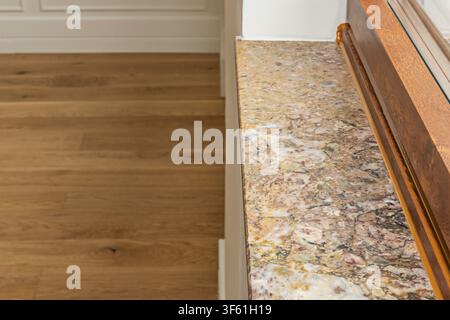 Warm-Toned Marble Countertop Edge Beside Wooden Floor and Cabinet Trim Stock Photo