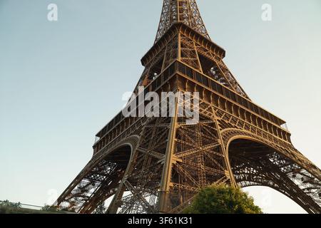Detailed low-angle view of the Eiffel Tower's iron lattice structure illuminated by warm late afternoon golden hour light. Stock Photo