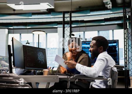 Cheerful team of engineers in inclusive office automating tasks with machine learning AI scripts. Smiling admin and coworker in wheelchair using artificial intelligence to do feature implementation Stock Photo