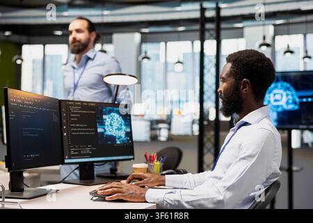 Computer scientist in office using AI automation scripts to reduce repetitive coding tasks. African american man using artificial intelligence technology in startup workspace Stock Photo