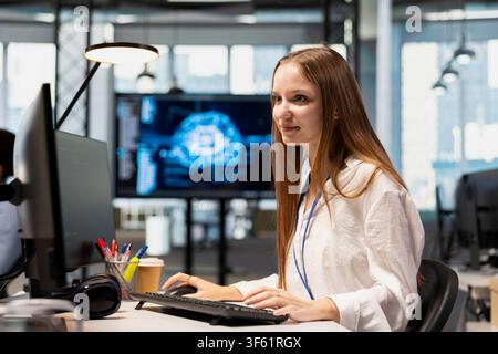 Cheerful junior dev in office using AI on computer to streamline app development. Joyous IT department intern at desk using PC to run debugging programs with machine learning technology Stock Photo