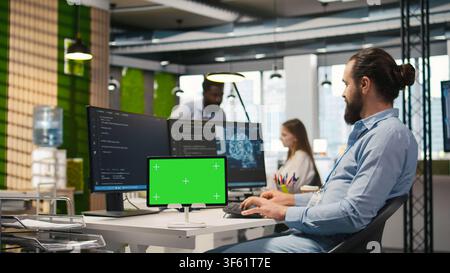 Technician developing applications using chroma key tablet, integrating AI next to office coworkers. Upbeat IT specialist debugging applications with isolated screen device , camera A Stock Photo