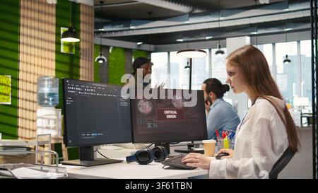 Female programmer in startup office struggling to fix application errors while coding. Young woman dealing with computer bugs while coding in software development agency, camera A Stock Photo