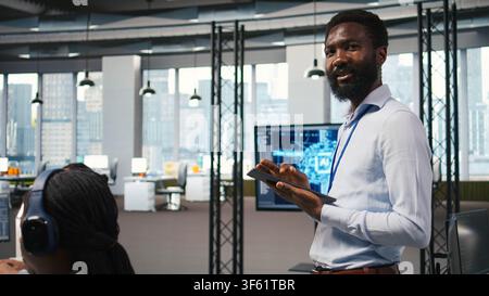 Joyous technician in office automating repetitive tasks using AI scripts. Upbeat man in workplace using artificial intelligence to speed up feature implementation, camera A Stock Photo