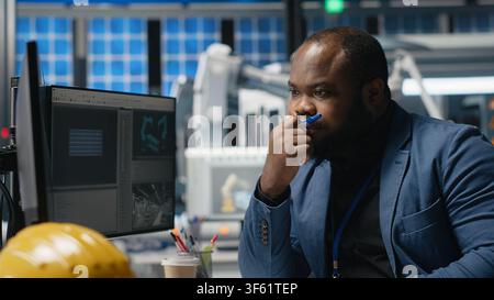 African american master engineer reviews operations in a solar tech plant, ensuring factory activity to meet green energy targets. Specialist uses tablet for manufacturing efficiency. Camera B. Stock Photo